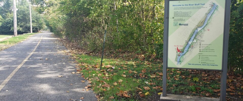 Paved trail next to row of trees with sign for River Bluff Trail