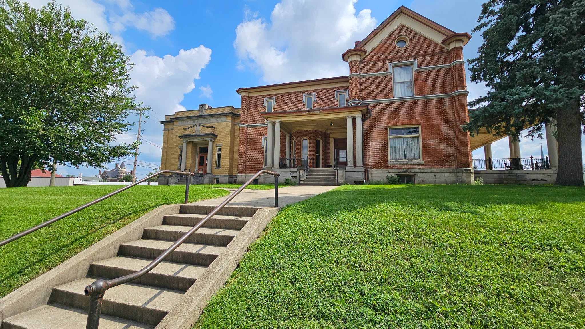 Street-level view looking up the steps toward the historic Memorial Center in Logansport, Indiana, with its red-brick exterior and columned porch.